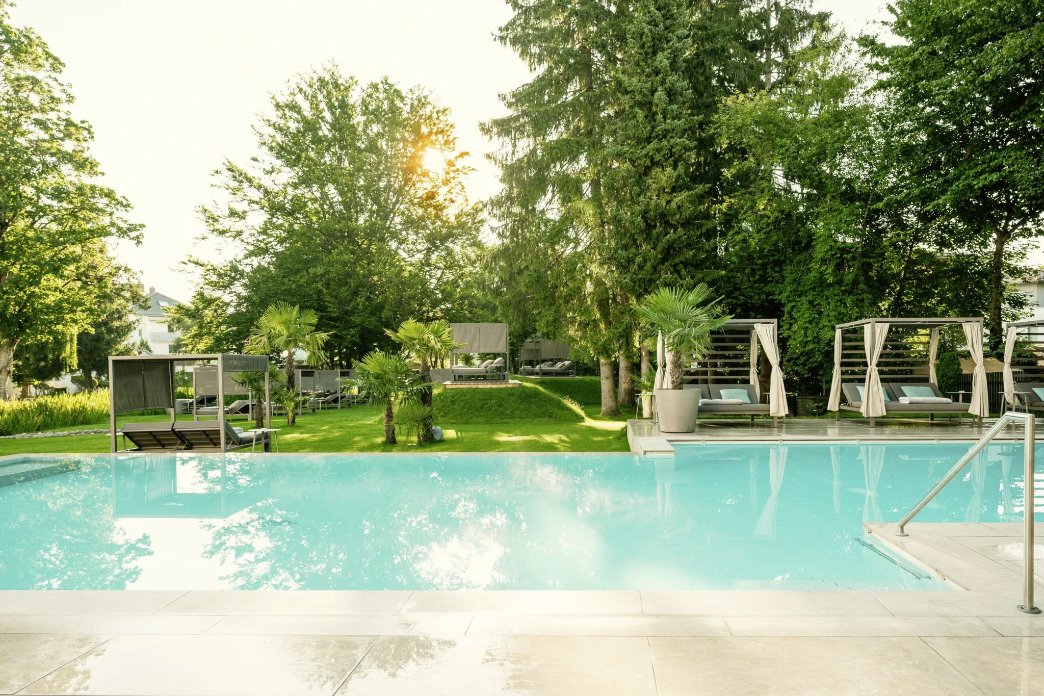 Outdoorpool im Das Parkhotel mit Blick in den Park mit Palmen und Daybeds