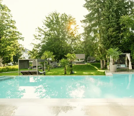 Outdoorpool im Das Parkhotel mit Blick in den Park mit Palmen und Daybeds
