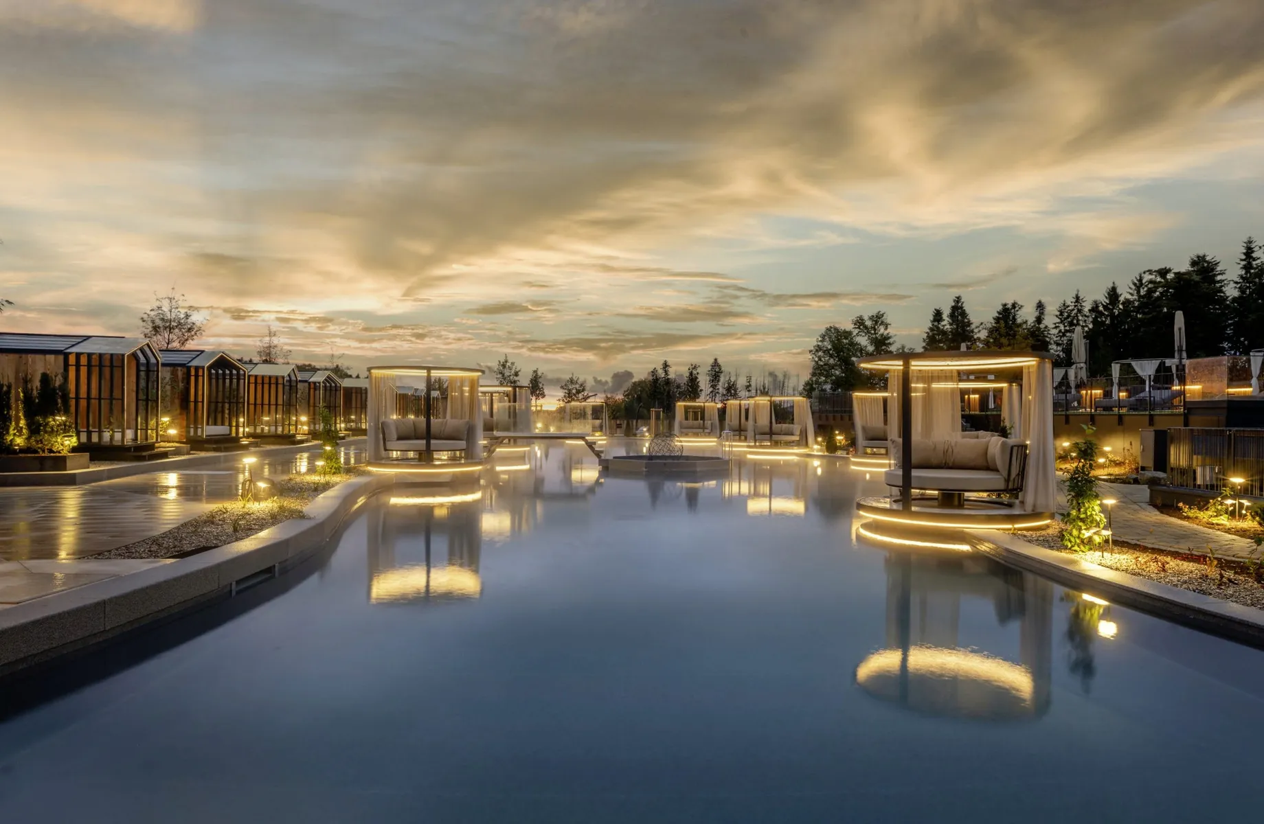Beleuchtete, schwimmende Inseln mit Daybeds im Naturteich des Wellnesshotels Das Stemp im Abendrot