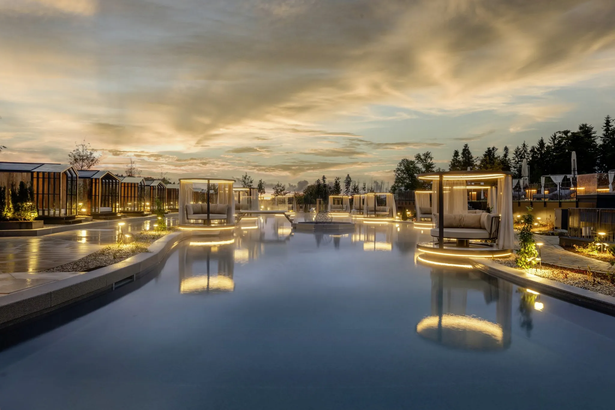 Beleuchtete, schwimmende Inseln mit Daybeds im Naturteich des Wellnesshotels Das Stemp im Abendrot