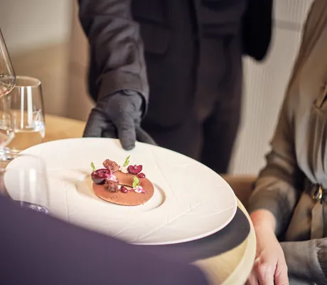 Bedienung mit schwarzem Handschuh serviert Gericht auf weißem Teller im Hotel Deimann