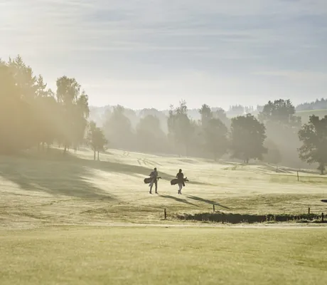zwei Golfer laufen im Frühnebel über den Golfplatz des Hotel Deimann
