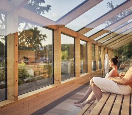 Paar sitzt mit weißen Handtüchern in der Panoramasauna im Hotel Deimann mit Glasdach