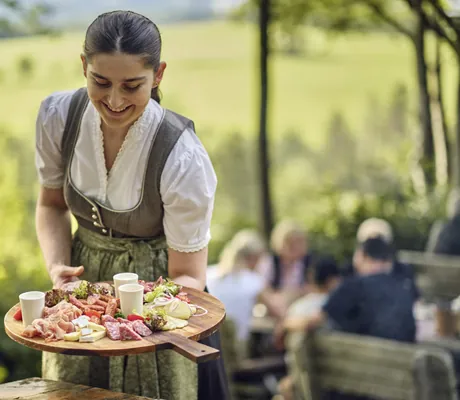 Bedienung in Dirndl päsentiert große Brotzeitplatte im Hotel Deimann