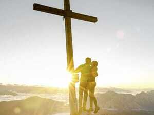 Paar steht küssend am Gipfelkreuz im Sonnenaufgang am Falkensteiner Kronplatz