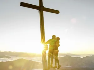 Paar steht küssend am Gipfelkreuz im Sonnenaufgang am Falkensteiner Kronplatz