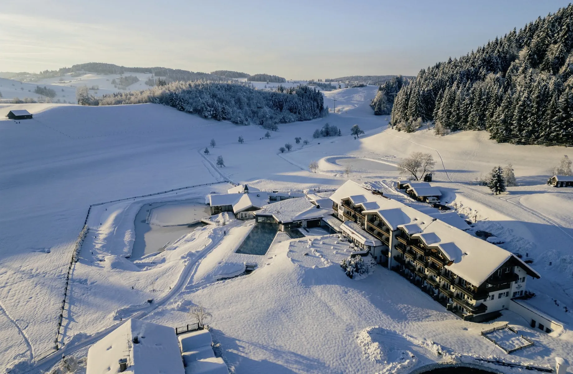 Luftaufnahme vom Wellnesshotel Haubers Naturresort mit Außenpool in verschneiter Allgäuer Landschaft