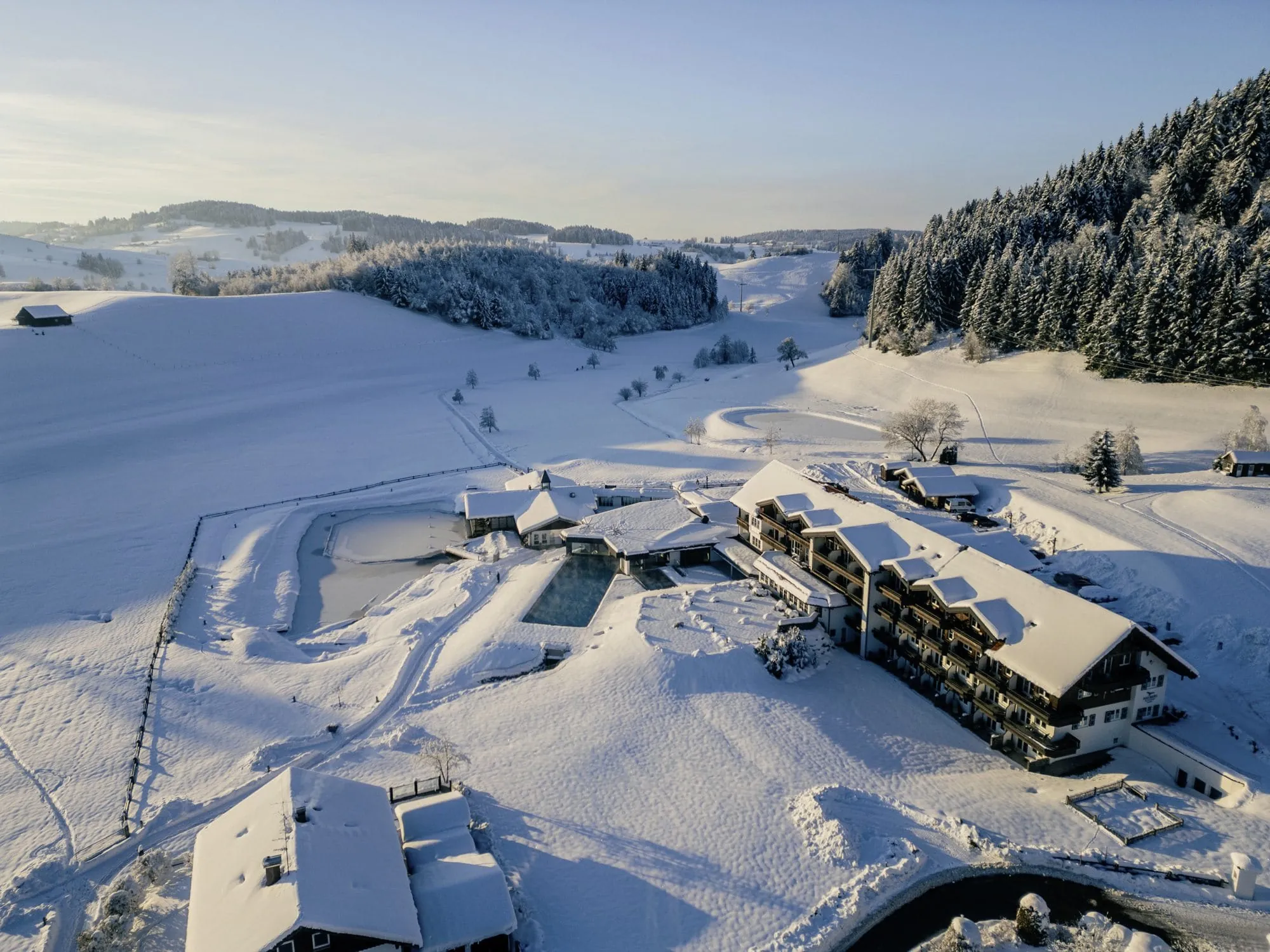 Luftaufnahme vom Wellnesshotel Haubers Naturresort mit Außenpool in verschneiter Allgäuer Landschaft