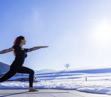 Frau praktiziert Yoga auf Terrasse mit verschneiter Allgäuer Bergkulisse im Wellnesshotel Haubers Naturresort