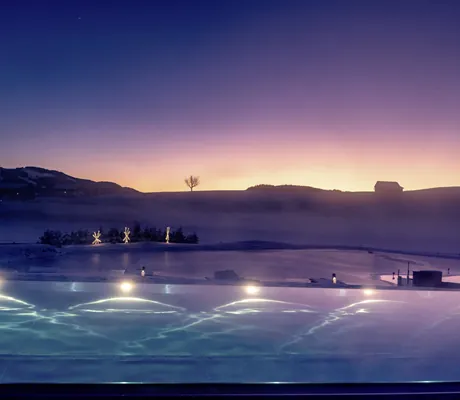 Beleuchteter Außenpool in der Abenddämmerung mit Bergpanorama im Wellnesshotel Haubers Naturresort in Oberstaufen
