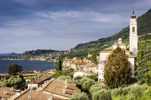 Blick auf die Altstadt von Gargnano am Gardasee in der Nähe des STROBLHOF LAKE GARDA – Active Family SPA Resort mit Kirchturm, Häusern mit roten Dächern und bewaldeten Hügeln im Hintergrund