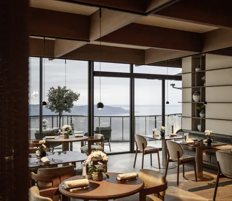 Modern eingerichtetes Restaurant des STROBLHOF LAKE GARDA Active Family SPA Resort mit Holztischen, Stühlen, großen Fenstern und Blick auf See und Berge