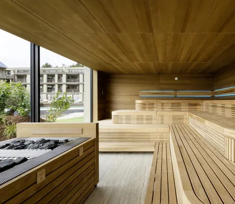 Sauna des STROBLHOF LAKE GARDA Active Family SPA Resort mit mehrstufigen Holzbänken und großen Fenstern mit Blick auf Hotelgebäude und Outdooranlage