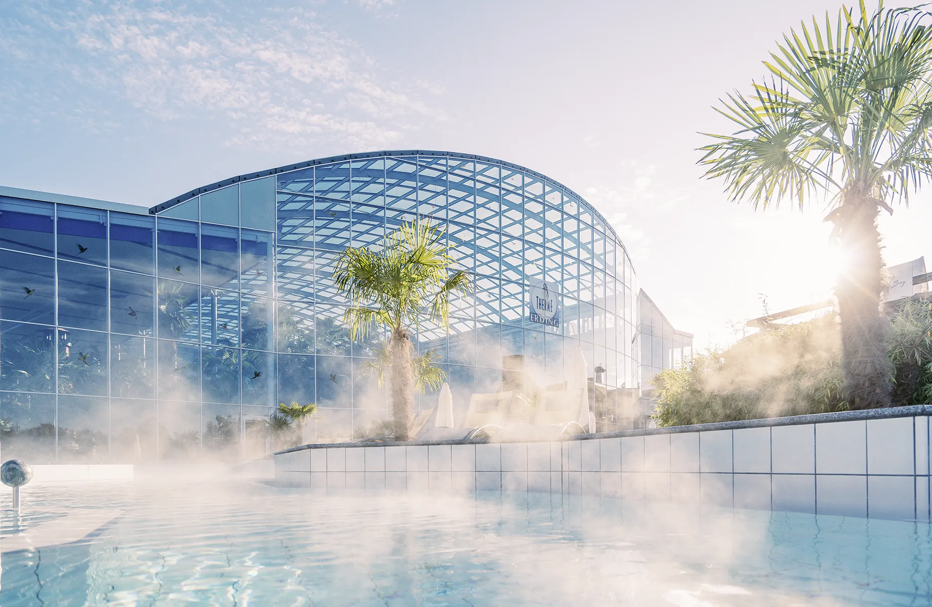 Blick auf das dampfende Outdoor-Wellenbad und die Außenansicht des Hotel Victory Therme Erding