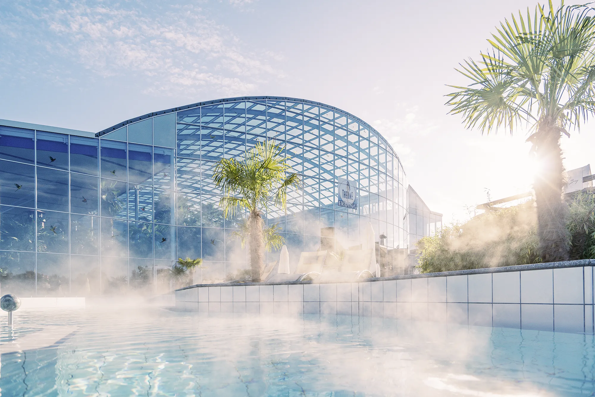 Blick auf das dampfende Outdoor-Wellenbad und die Außenansicht des Hotel Victory Therme Erding
