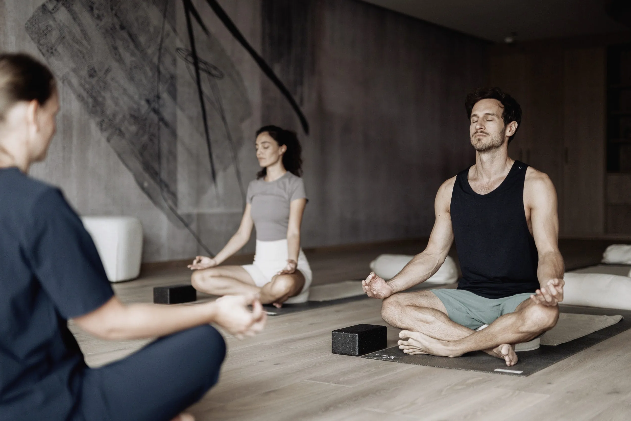 Mann und Frau in Sportkleidung sitzen im Yograraum vor der Yogalehrerin im Hotel Solvie