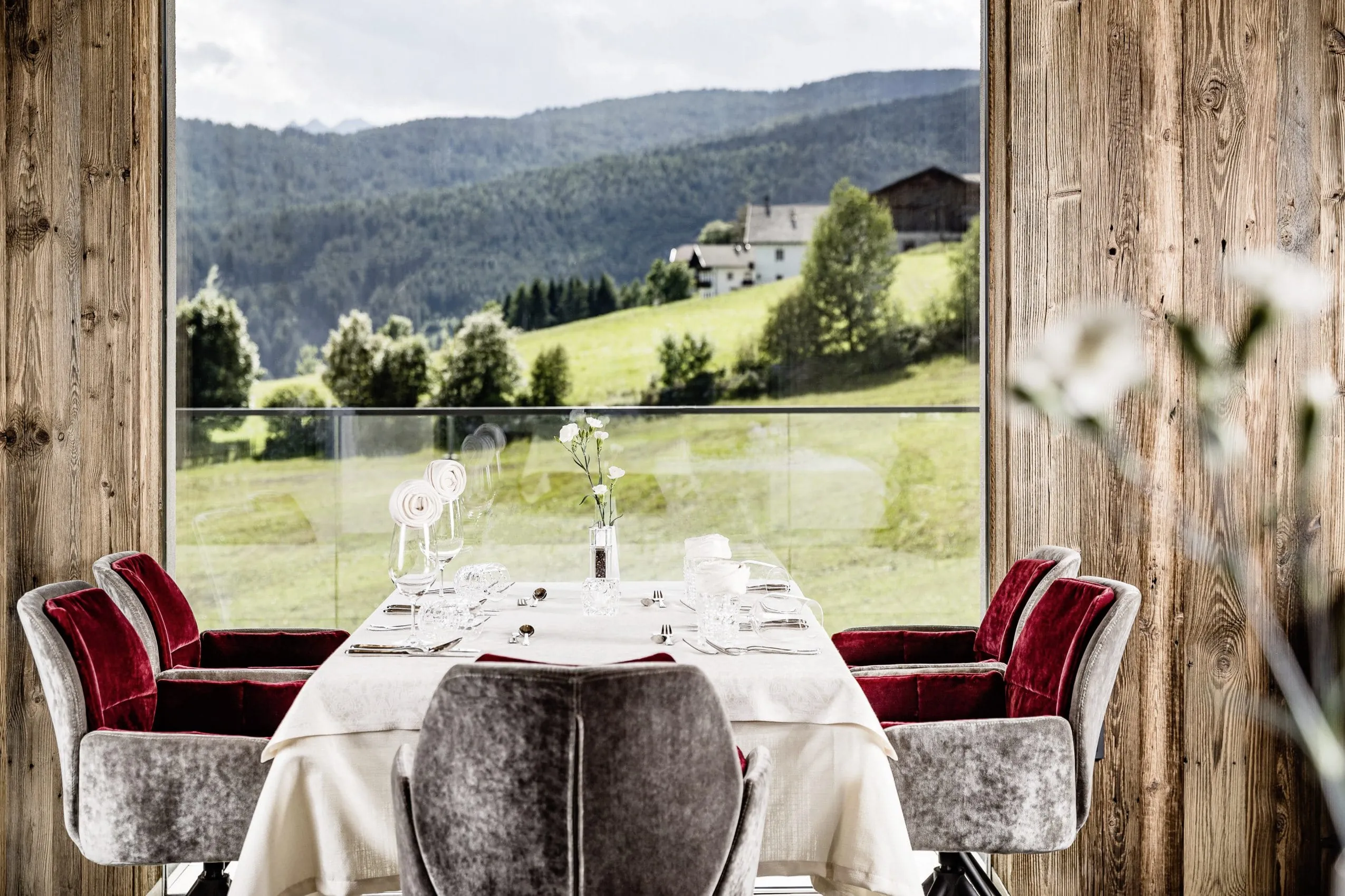 gedeckter Tisch im Restaurant des Sonnenberg Meransen mit grauen Samtsesseln und Blick auf die Wiese
