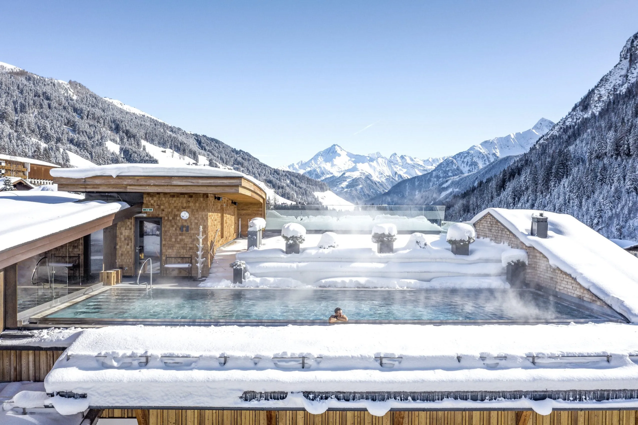 Mann liegt im Rooftop-Pool des Alpin SPA Hotel Tuxerhof im tiefen Winter bei strahlendem Sonnenschein