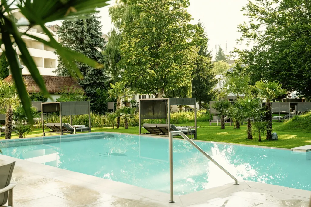 Outdoorpool im Das Parkhotel mit Blick in den Park mit Palmen und alten B&auml;umen