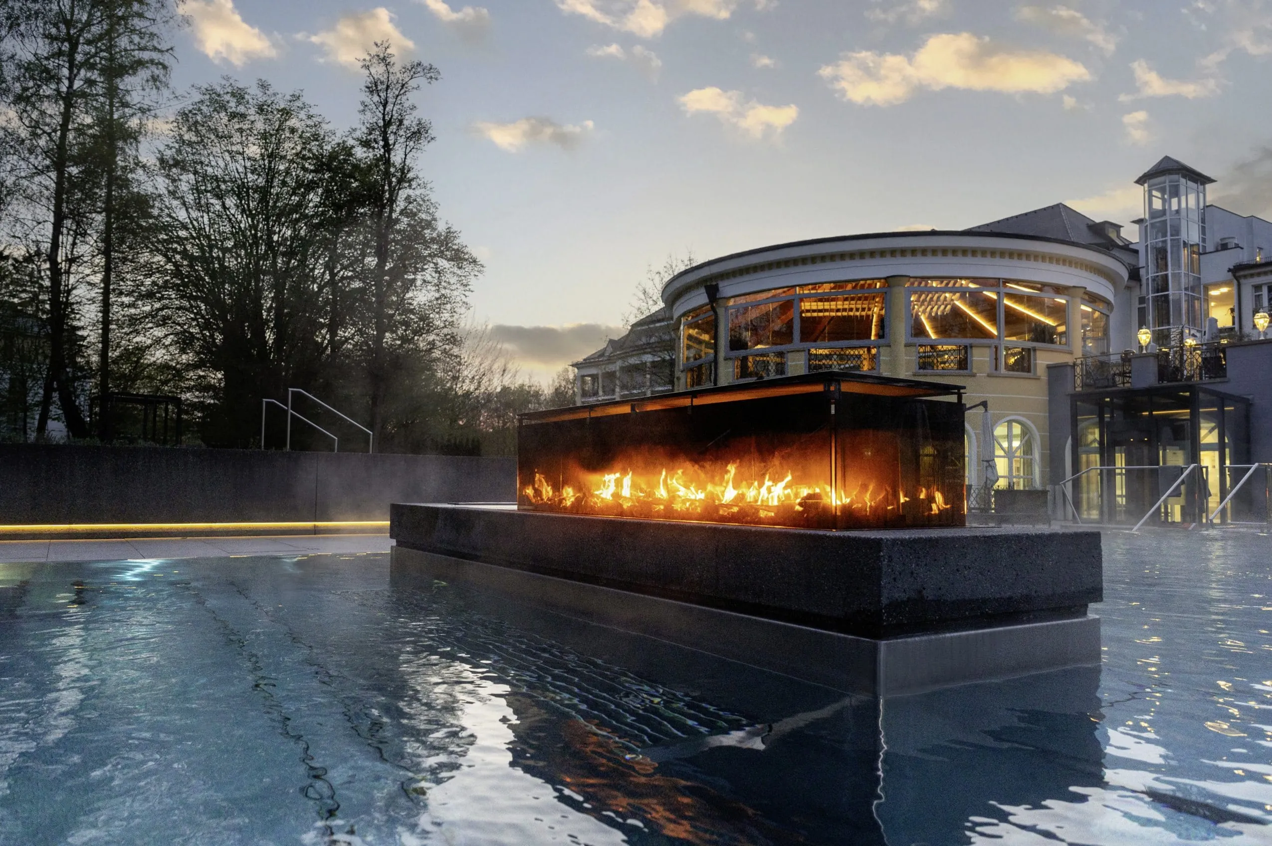 Feuerstelle im Outdoorpool des Wellnesshotels Der Sonnenhof, im Hintergrund die Abend&auml;mmerung