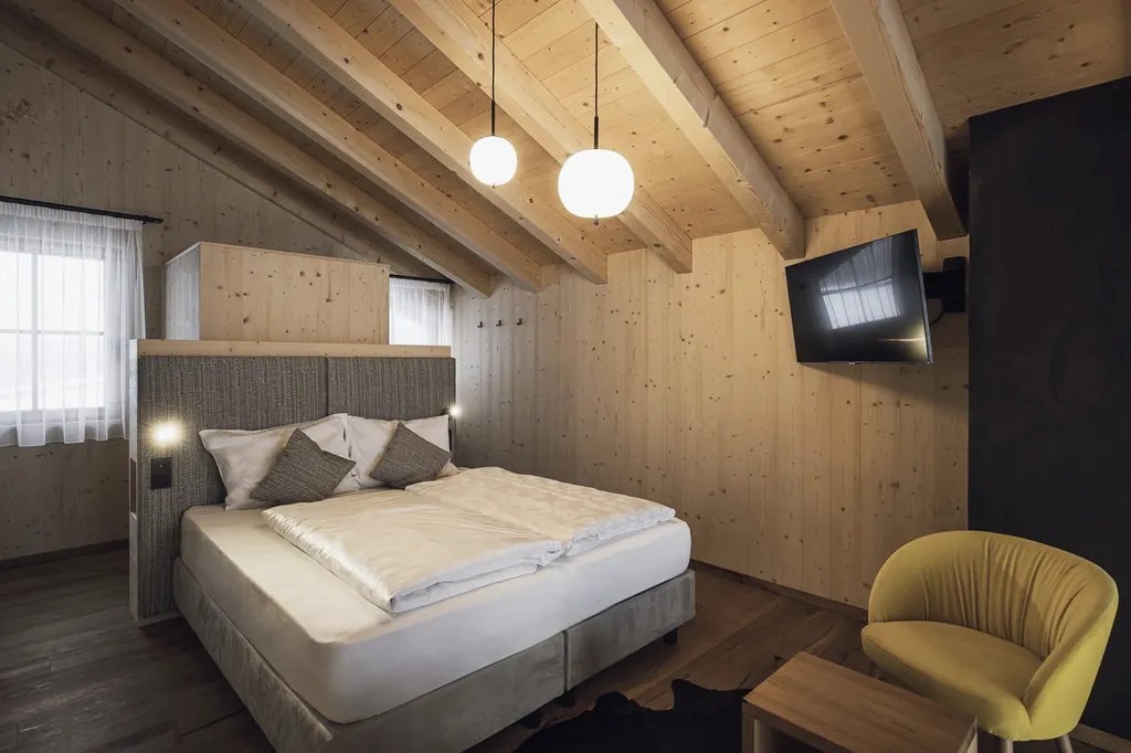 Doppelbett im Schlafbereich in Kesslers Mountain Lodge mit hoher Holzdecke und gelbem Sessel