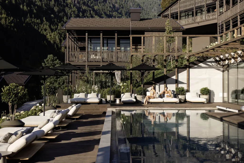 Pärchen auf weißen Liegen unter schwarzen Sonnenschirmen am Outdoorpool in den Amonti Chalets