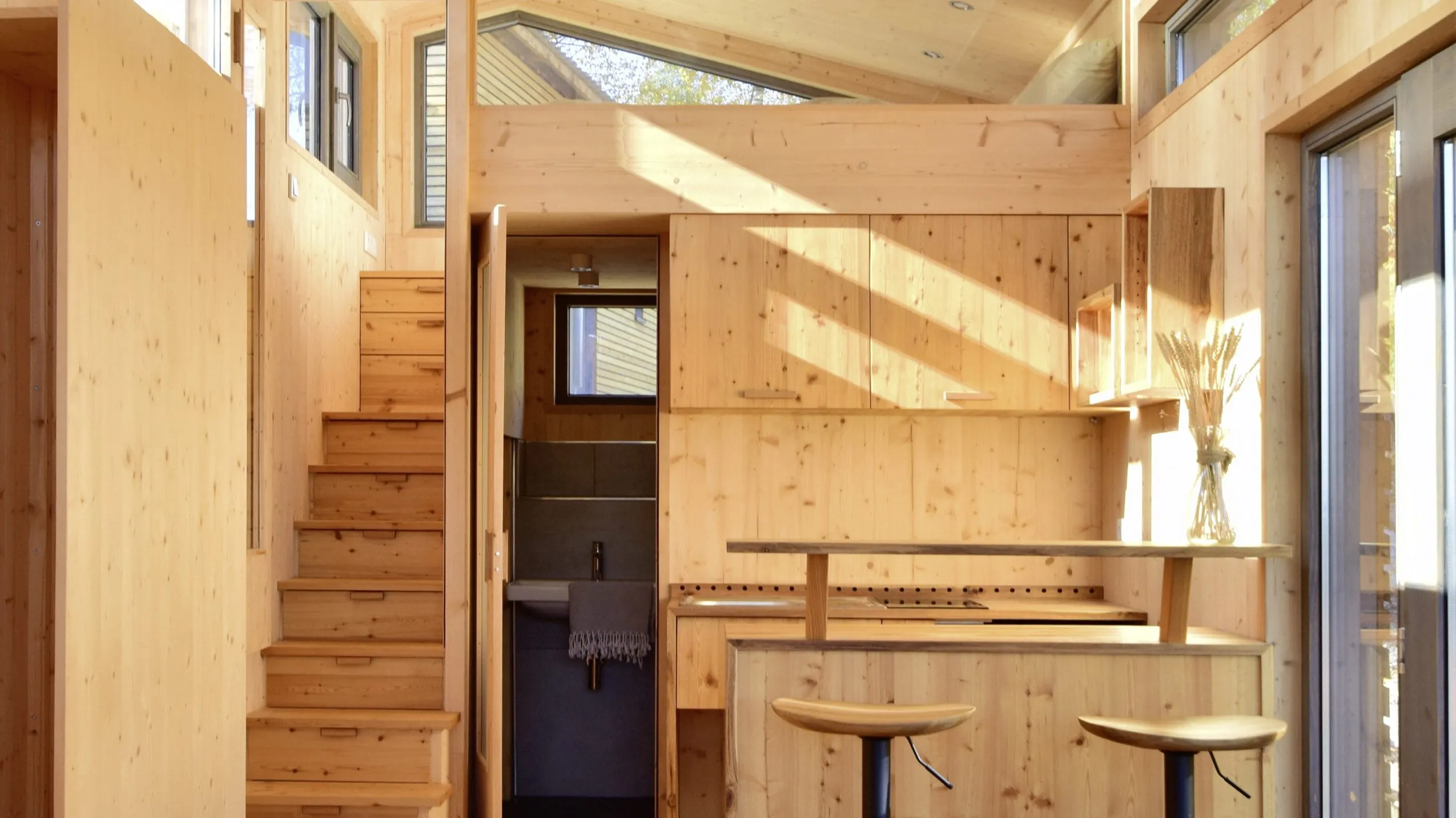 Helle Holz-K&uuml;che im Tiny House des SEINZ Wisdom Resorts mit zwei Barhockern, Treppe und gro&szlig;z&uuml;gigem Tageslicht