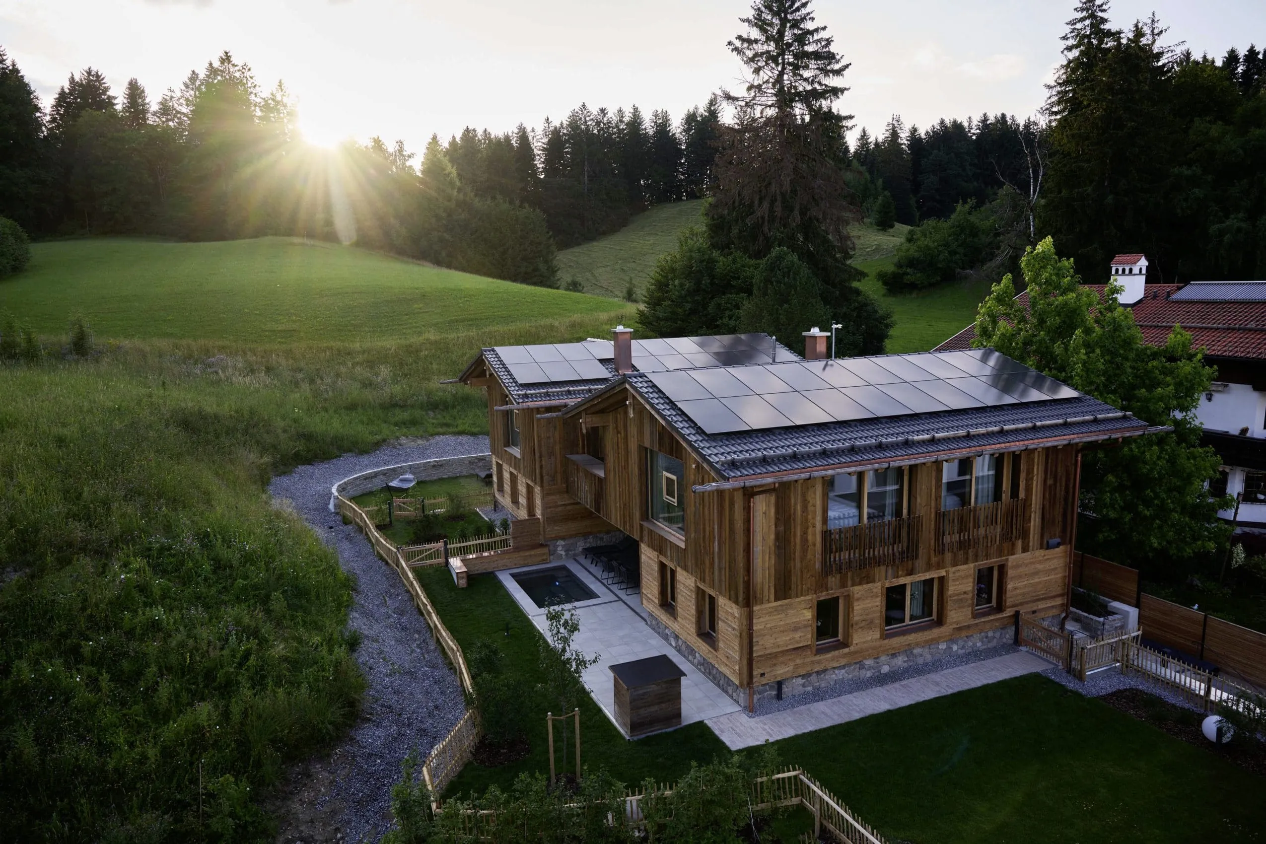 Blick auf die Ziegelberg Chalets mit Solarpaneelen auf dem Dach, umgeben von Wiesen und B&auml;umen bei Sonnenuntergang