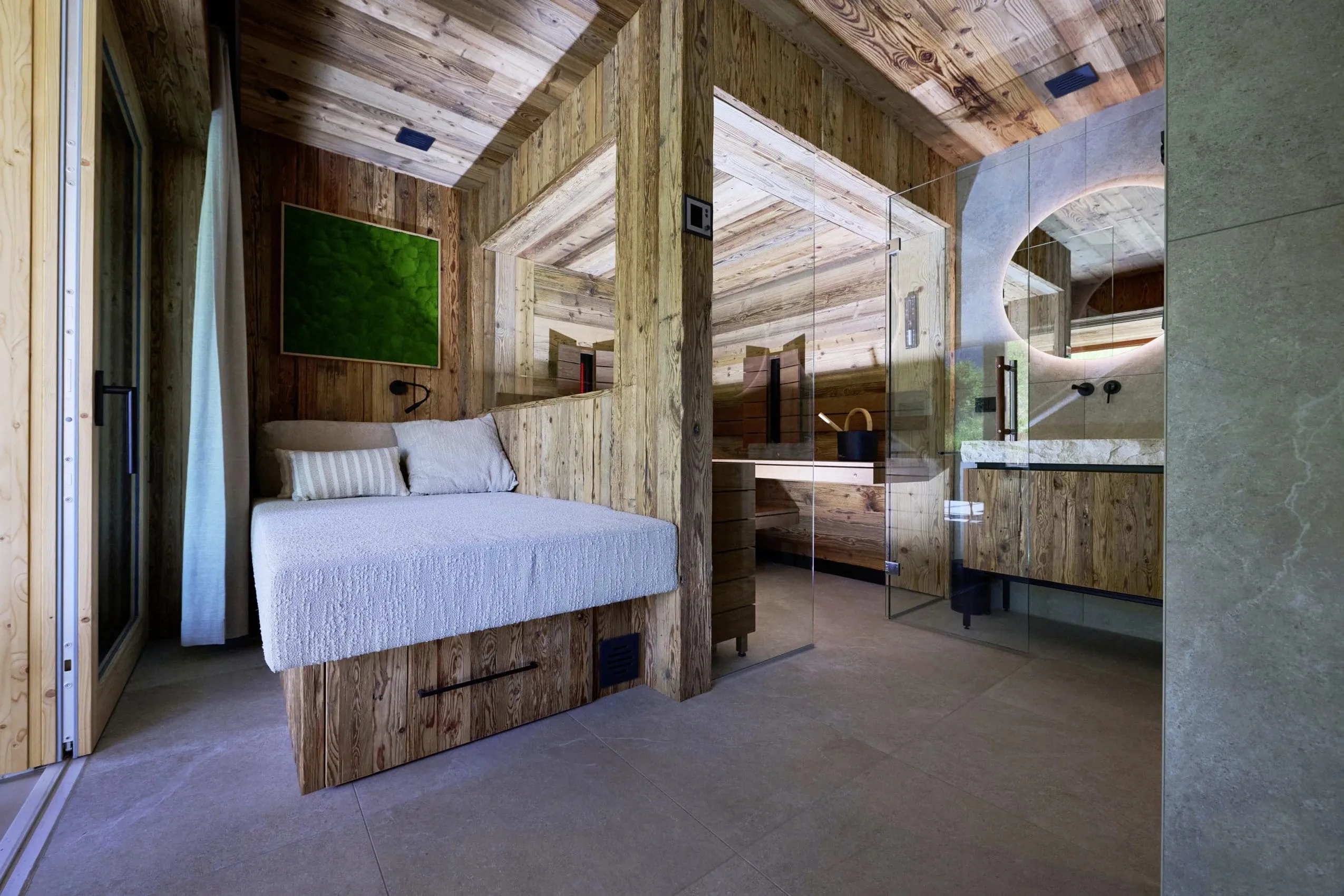 Modern eingerichteter Bereich der Ziegelberg Chalets mit Holzw&auml;nden, einer gem&uuml;tlichen Sitzbank, Sauna und rundem Spiegel &uuml;ber Stein-Waschbecken