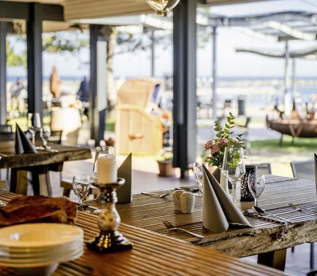 gedeckter Holztisch im Restaurant mit Terrasse und Meerblick im Damp Ostsee Resort