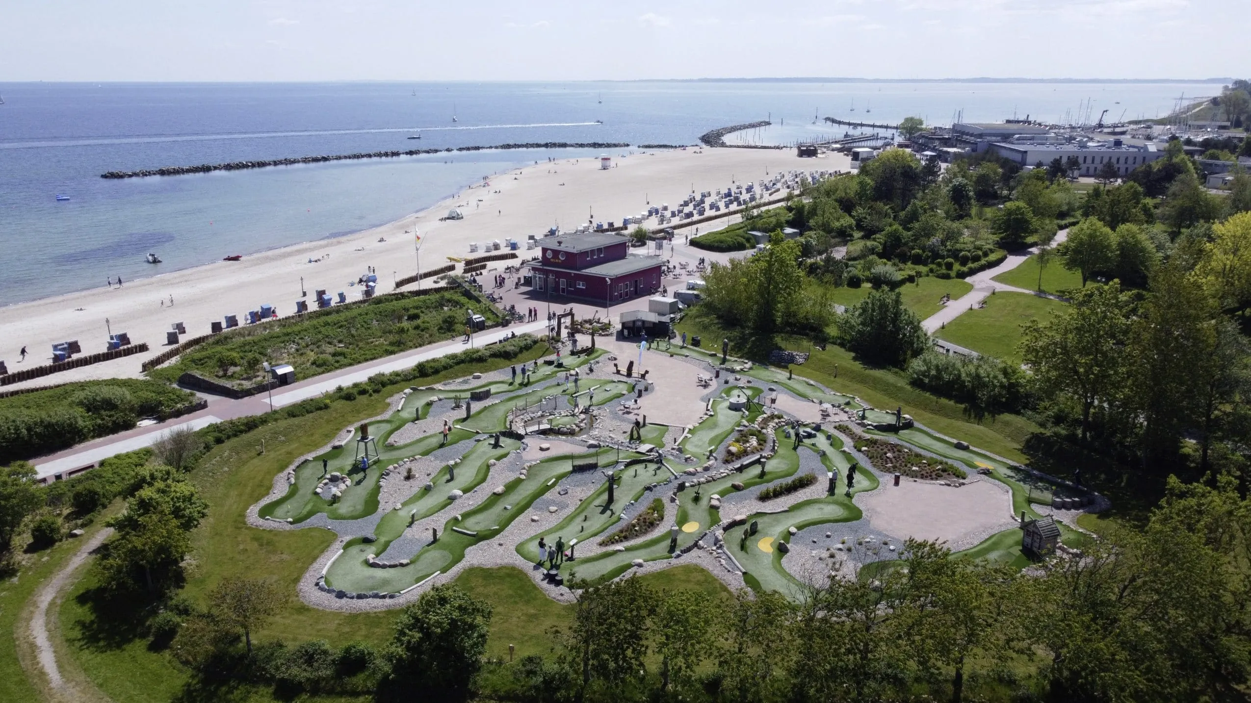 Luftaufnahme des Adventure-Minigolfplatzes direkt am Strand des Ostsee Resorts Damp, mit Meer, Strandk&ouml;rben und Promenade im Hintergrund