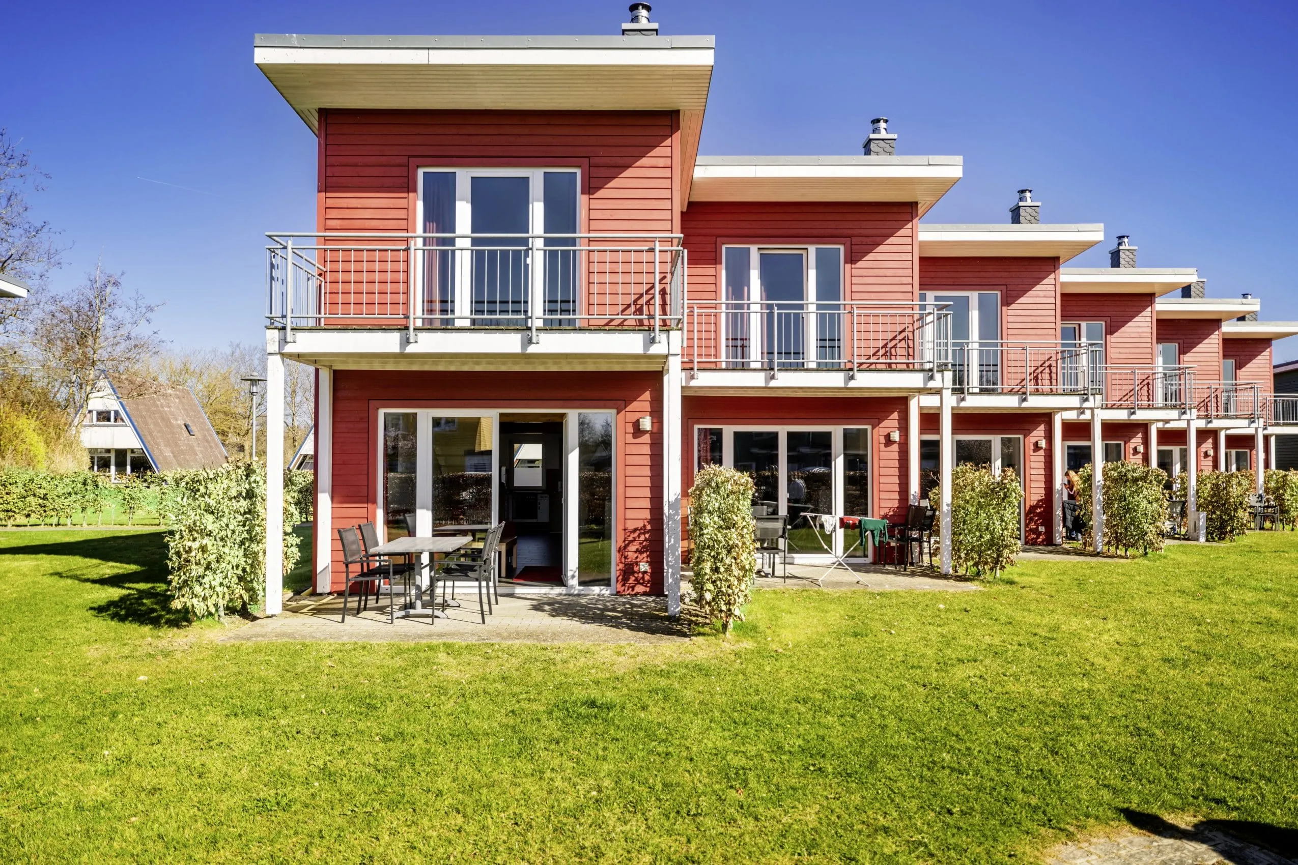 Rote, zweigeschossige Premiumh&auml;user mit Balkonen und Terrassen im Ostsee Resort & Ferienpark, umgeben von gepflegtem Rasen