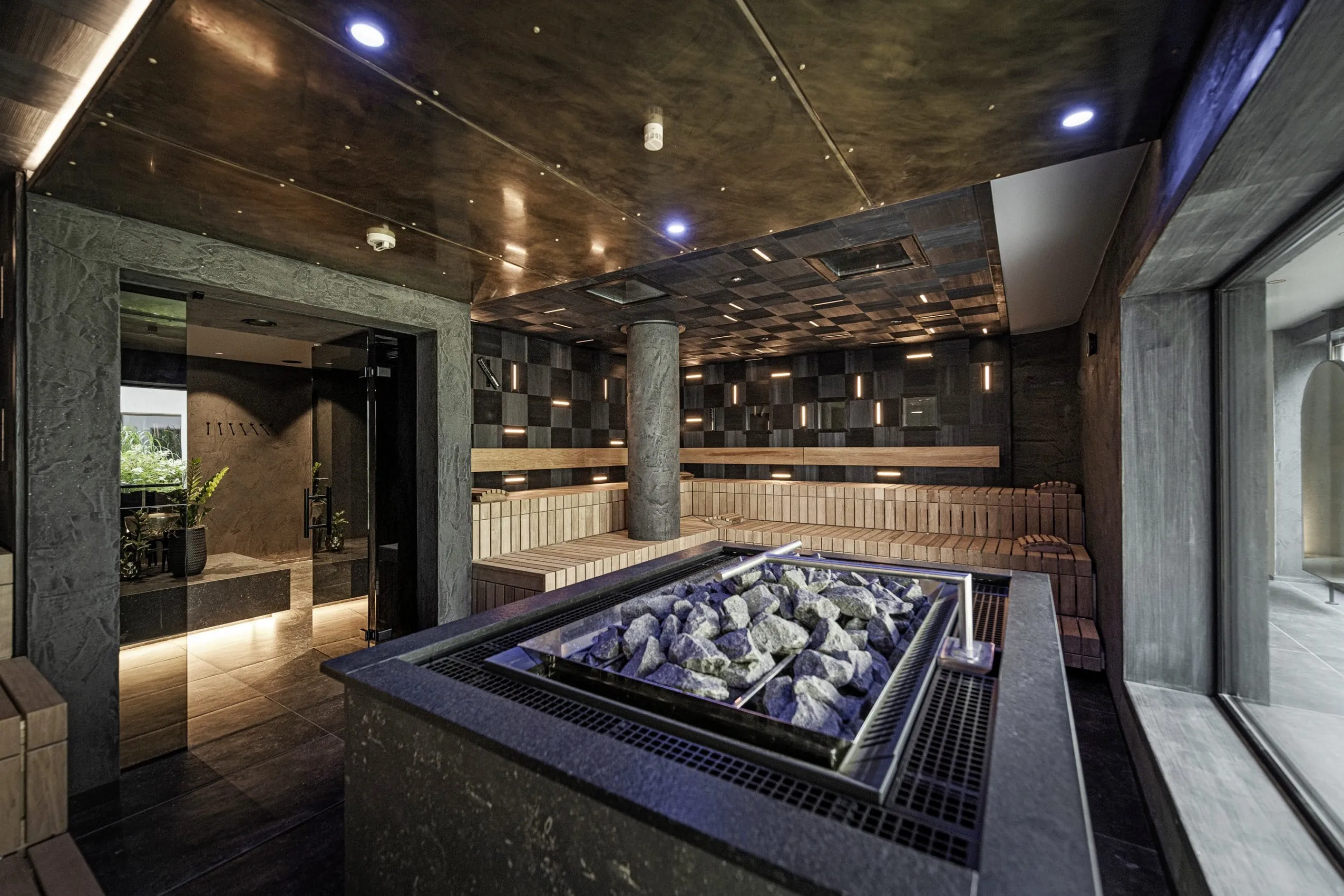 Moderne Sauna im Alpenresort Schwarz mit zentralem Saunaofen, Holzbankreihen und stilvoller Beleuchtung