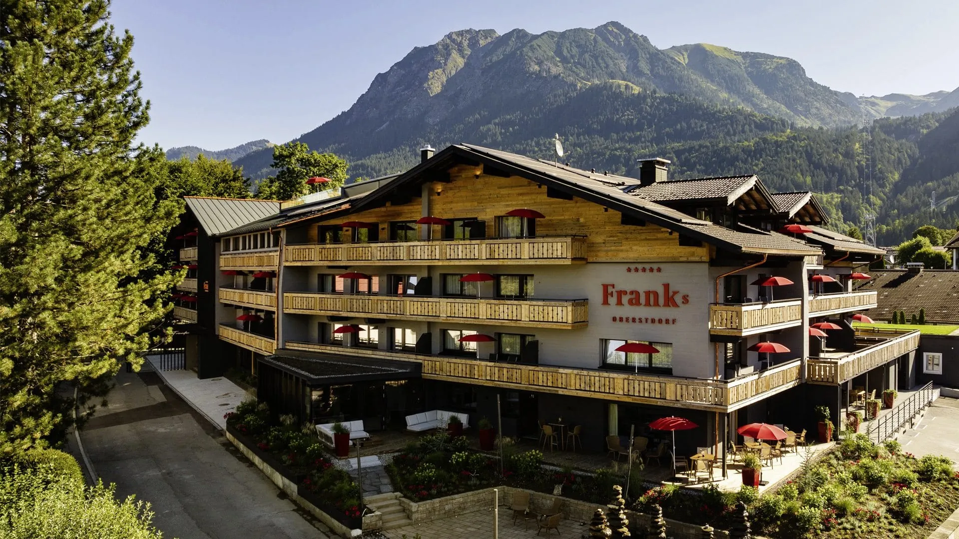 Traditionelles Hotel Franks mit Holzfassade und roten Sonnenschirmen vor Bergkulisse
