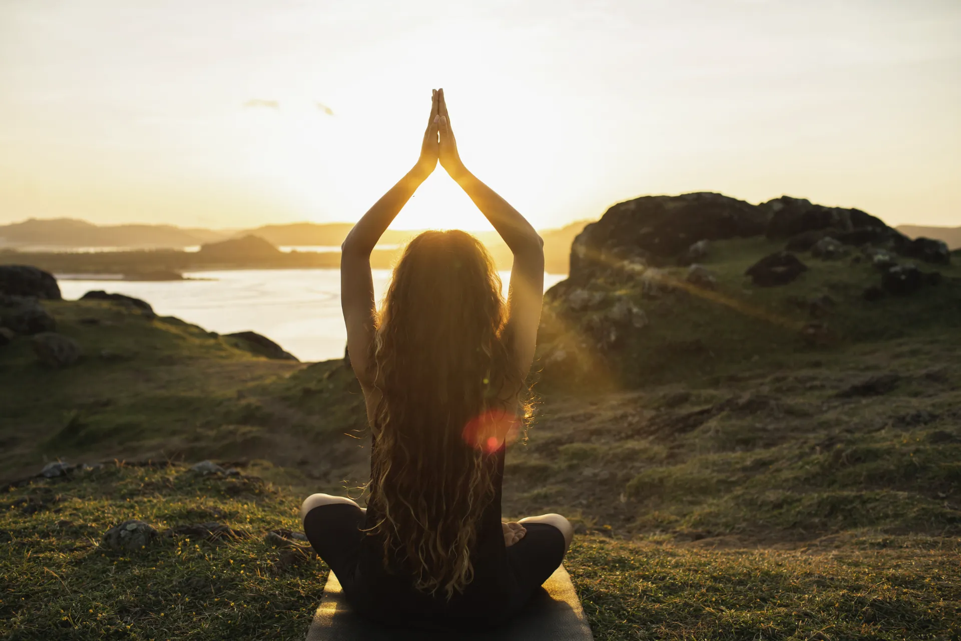 Frau bei Yoga vor Sonnenaufgang auf einer Wiese mit Blick auf Berge und Wasserlandschaft in der N&auml;he des Hotel Franks