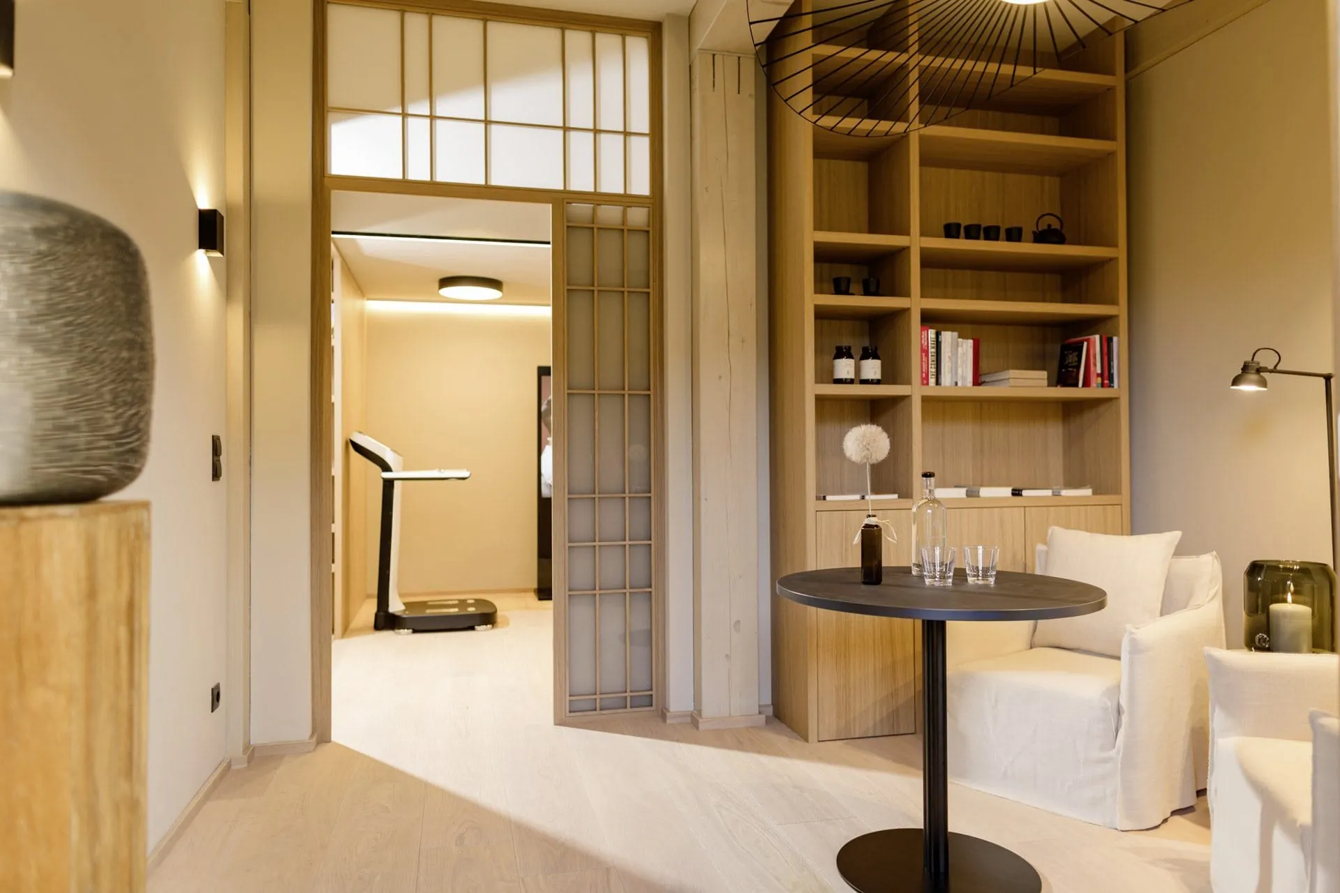 Stilvoll eingerichtetes Longevity Lab im Posthotel Achenkirch mit hohem Holzregal, Sesseln, rundem Tisch und Blick auf eine Waage im Hintergrund