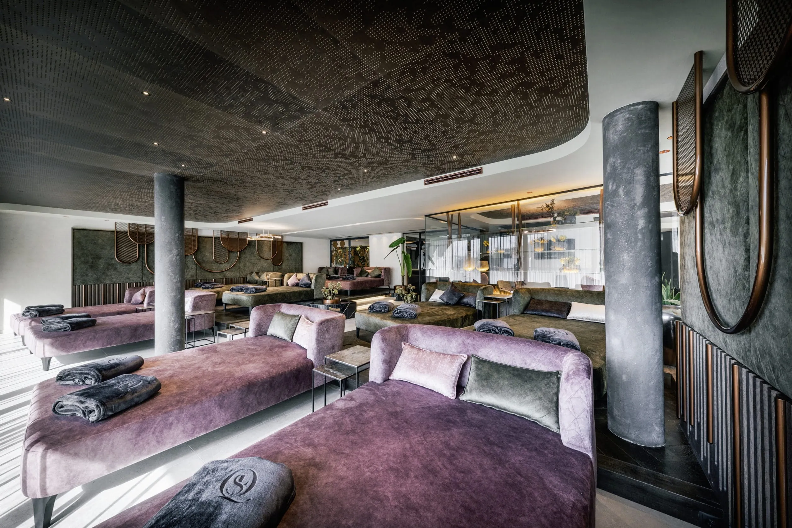 Eleganter Ruheraum in der Quellenhof See Lodge mit stilvollen lila und grauen Liegen und gefalteten Decken mit Logo