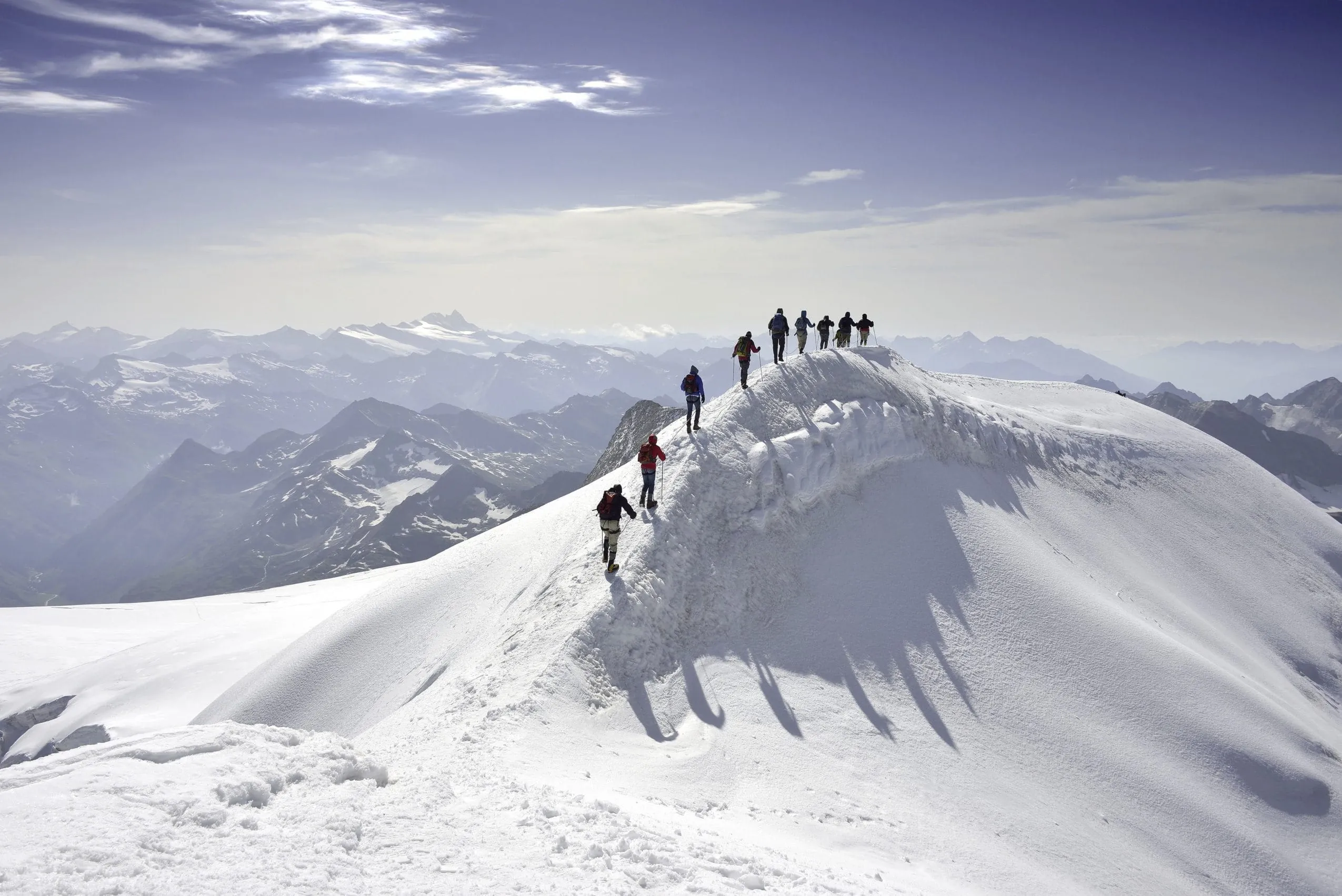Gruppe von Wanderern auf einem schneebedeckten Bergr&uuml;cken in der N&auml;he des Wanderhotel Gassner mit Blick auf die umliegenden Alpengipfel unter klarem Himmel