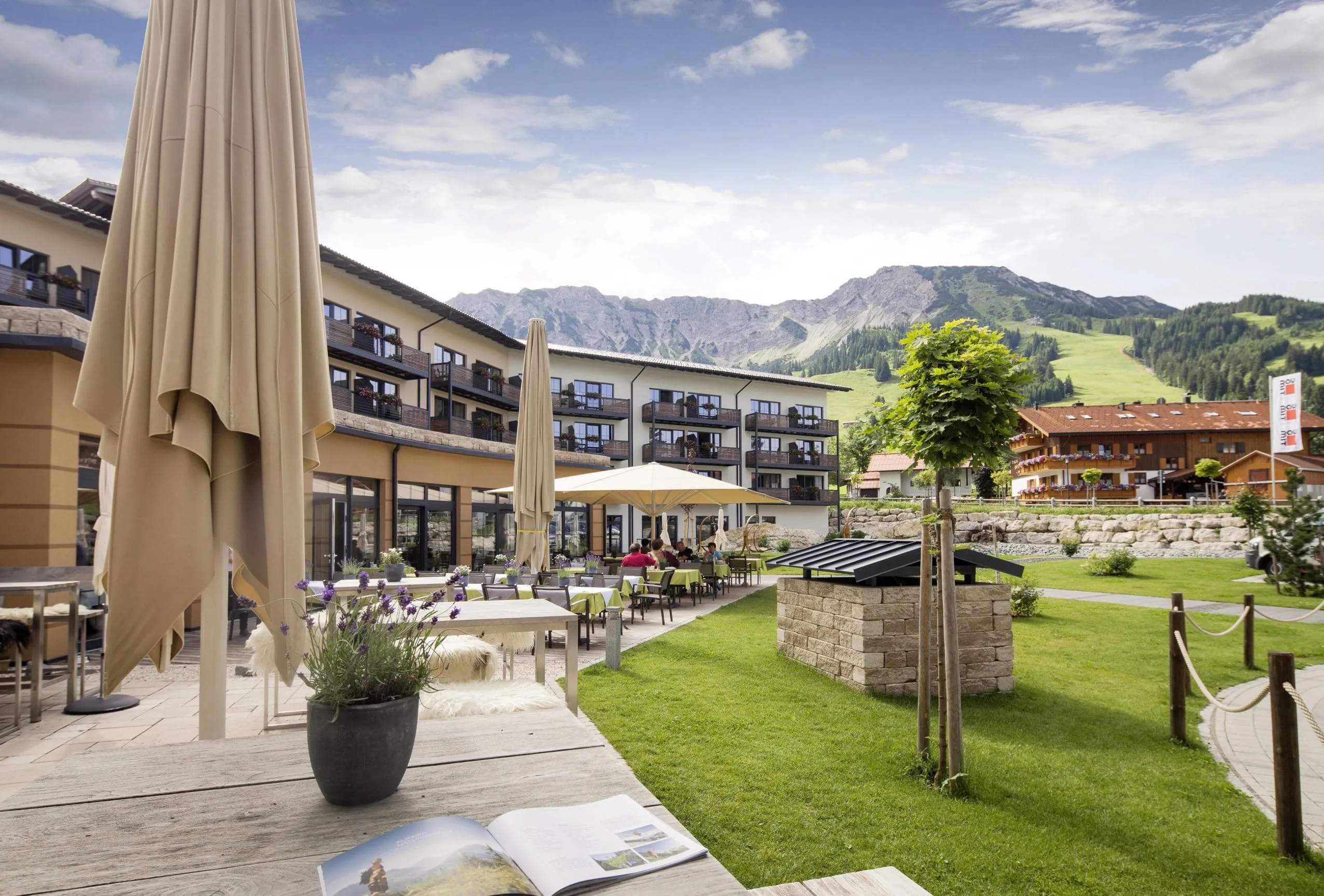 Au&szlig;enansicht des Panoramahotels Oberjoch mit Terrasse, Sonnenschirmen, gr&uuml;ner Gartenanlage und Bergen im Hintergrund