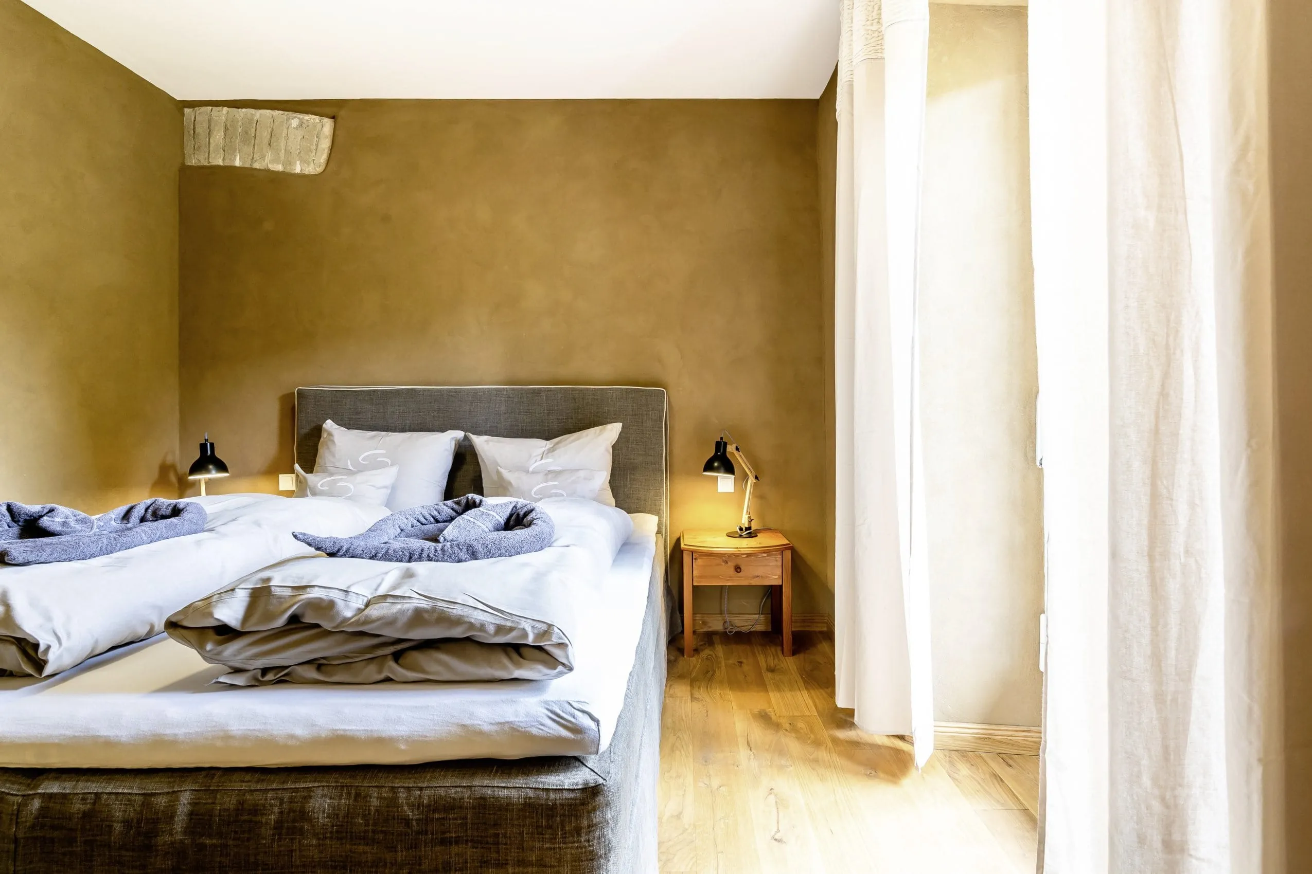 Zimmer im SEINZ Wisdom Resort mit freigelegter Mauer an der Wand und Leinenvorh&auml;ngen