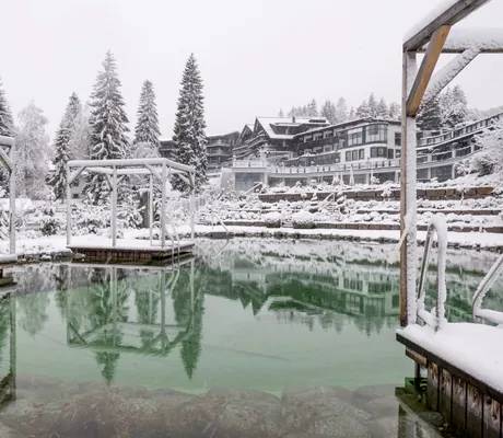 Verschneiter Naturbadesee des Alpin Resort Sacher Seefeld mit Holzplattformen und umliegender Winterlandschaft