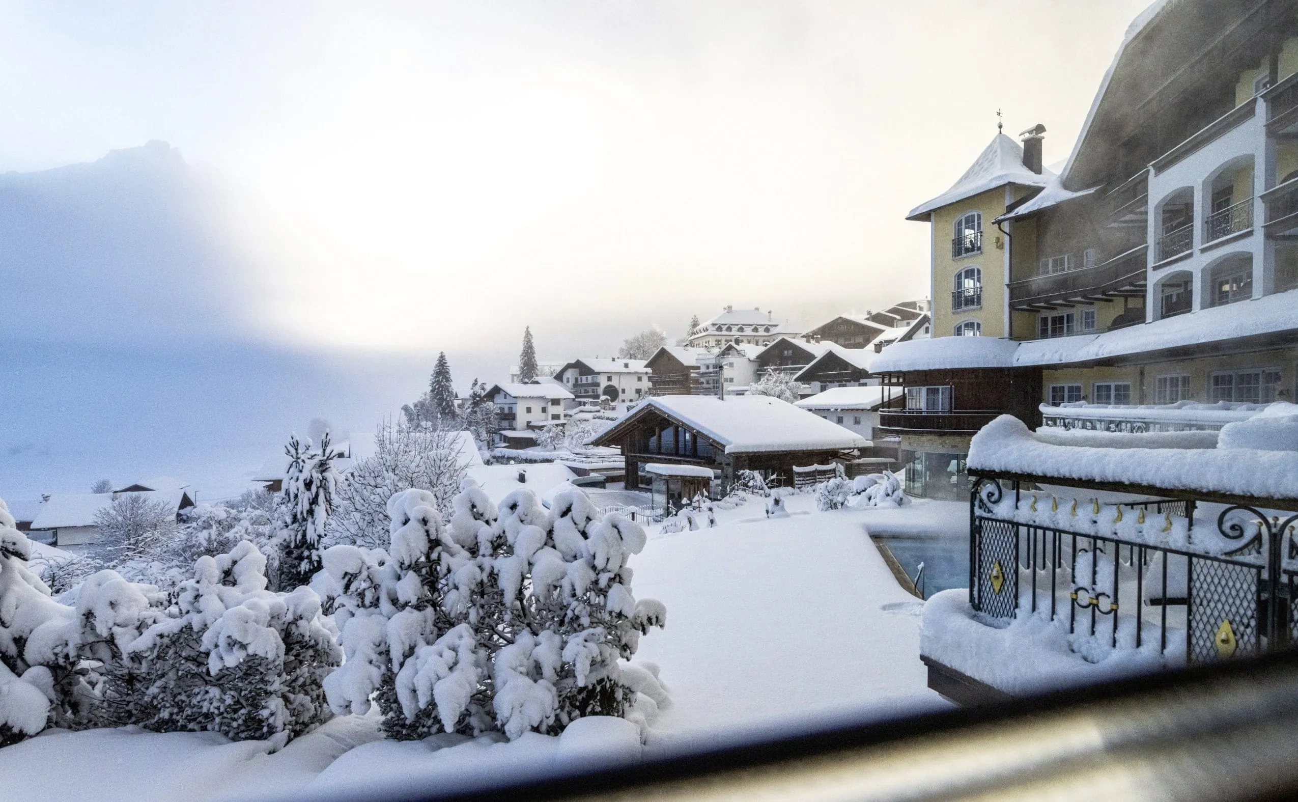 Fassade des Hotel Post Lermoos mit gelbem Turm im tiefen Schnee und Blick auf Zugspitze im Nebel