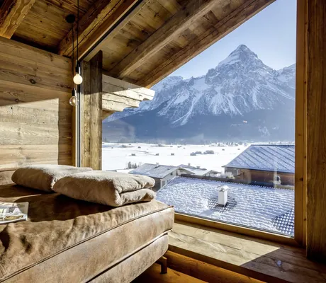 braune Lederliege im Hotel Post Lermoos unter dem Holzdach mit Blick auf verschneite Berge