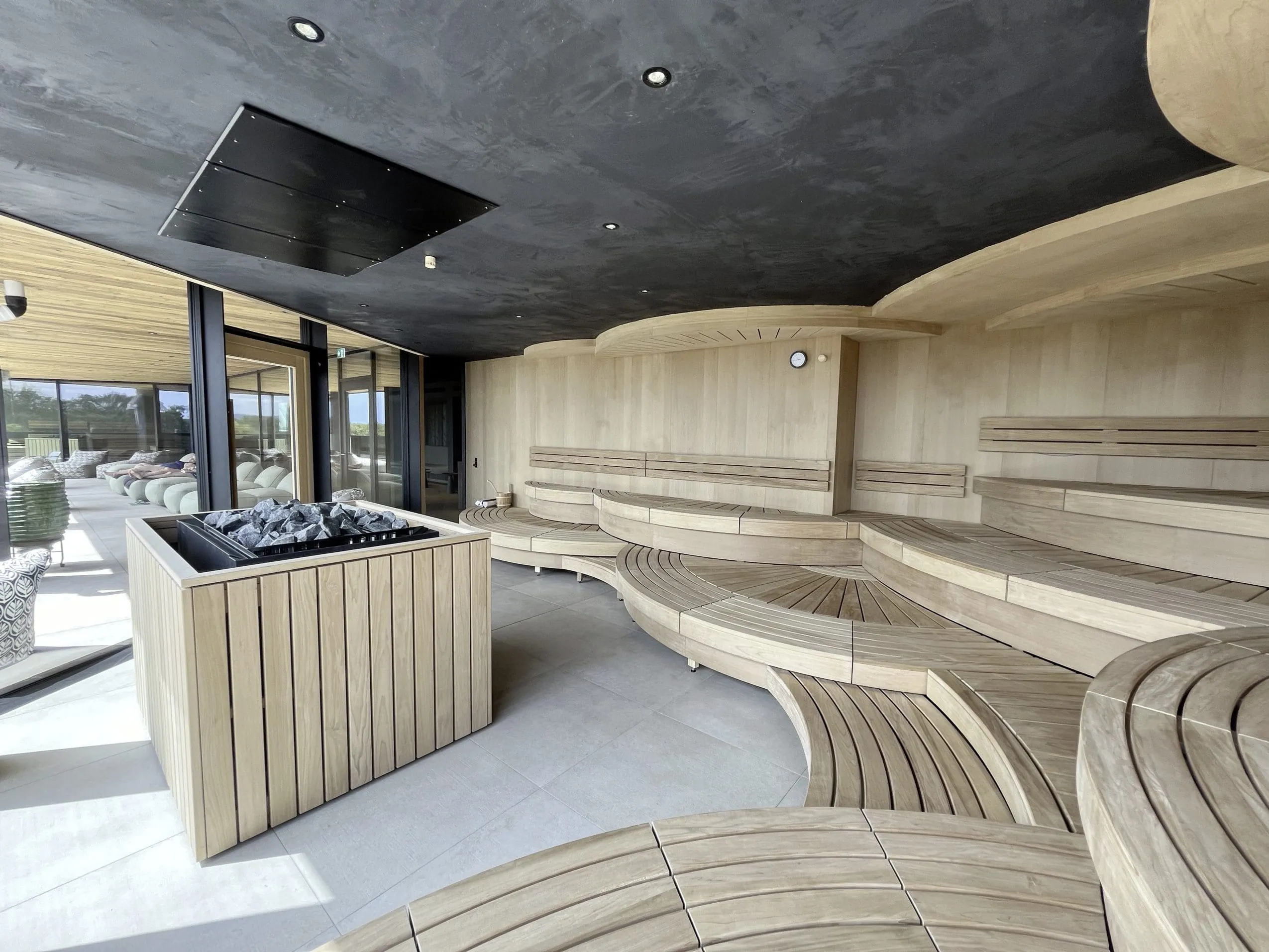 Eventsauna mit runden Sitzb&auml;nken und Blick zum Ruhebereich im DAS M&Uuml;HLBACH | thermal retreat & wellness resort