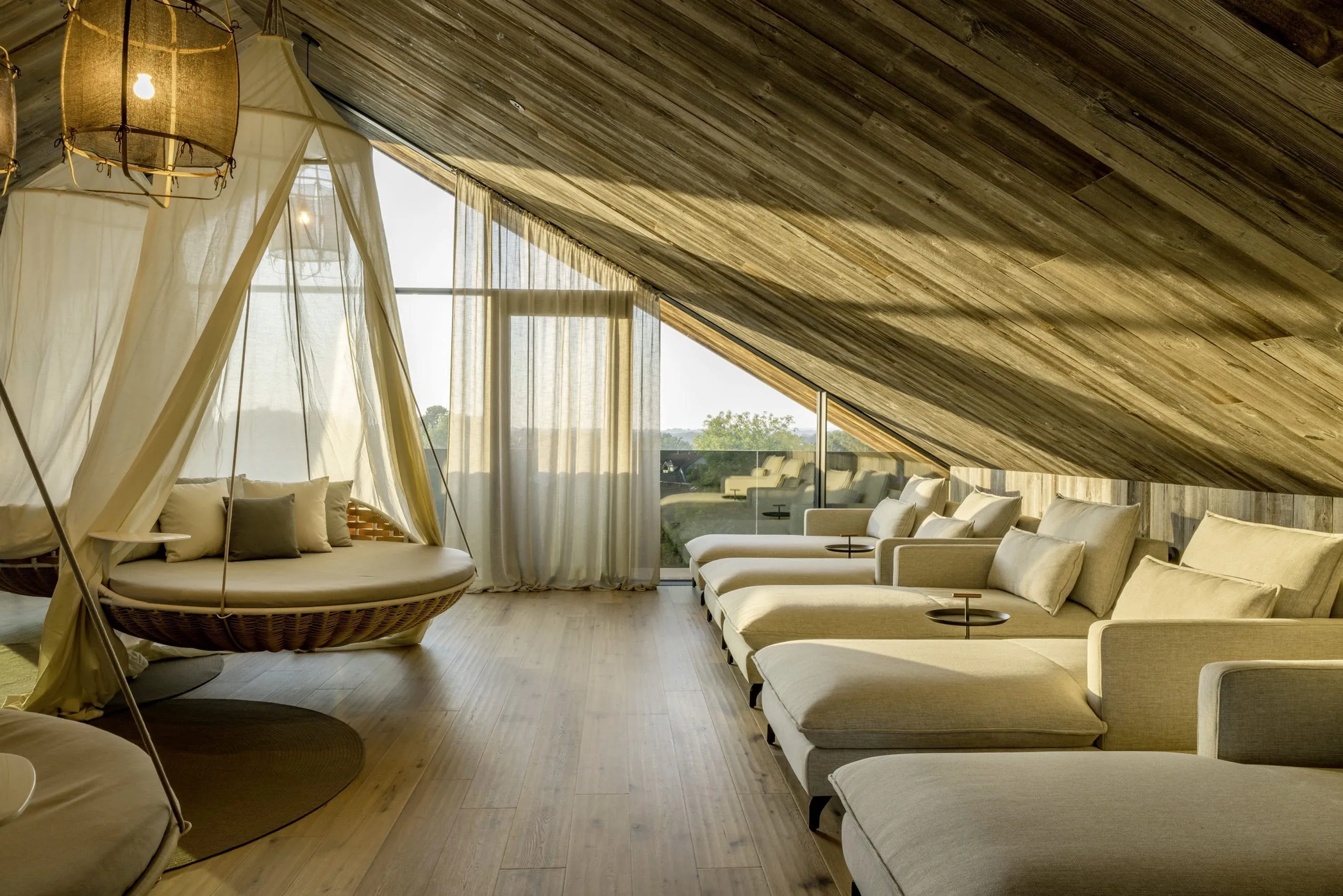 Ruheraum im DAS M&Uuml;HLBACH | thermal retreat & wellness resort unter dem Dach mit H&auml;ngeschaukeln und mehreren beigefarbenen Liegen