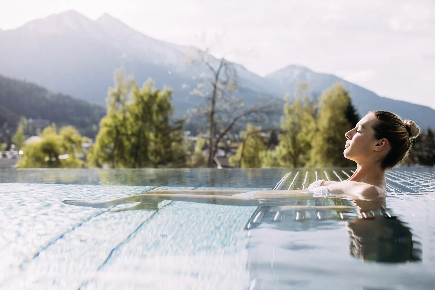 Frau entspannt auf einer Liegefl&auml;che im Outdoorpool des Wellnesshotel Alpin Resort Sacher Seefeld &ndash; Tirol mit Bergpanorama im Hintergrund