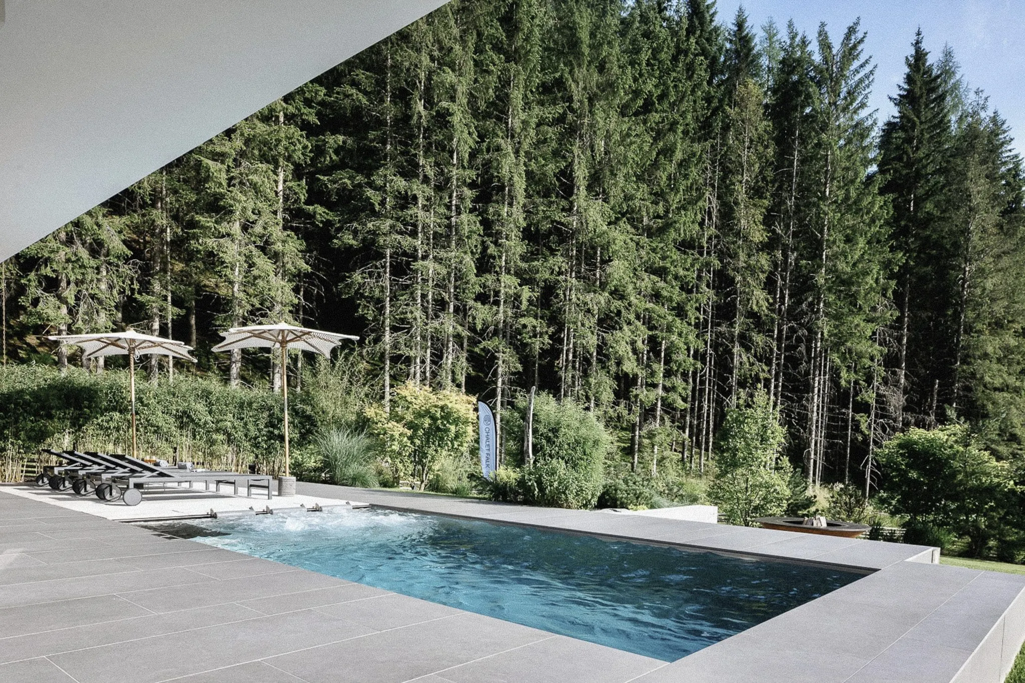 Au&szlig;enpool mit Sonnenliegen und Blick in den Wald im Chalet Falk