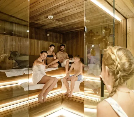 Familie in der Familiensauna des Familotel Zauchenseehof mit Holzverkleidung und Glasfront