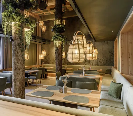 Stilvoll eingerichtetes Restaurant mit Holzdekor, grünen Polstermöbeln und hängenden Designer-Leuchten im Familotel Zauchenseehof