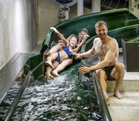 Mädchen und ihre Mutter rutschen lachend eine grüne Wasserrutsche im Familotel Zauchenseehof hinunter, der Vater sitzt daneben